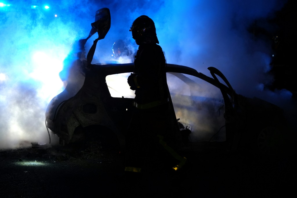 رجل إطفاء يسير قرب سيارة متفحمة بعدما أحرقها متظاهرون في ضاحية نانتير في غرب باريس في 27 حزيران/يونيو 2023 بعد قتل شرطي لمراهق عند نقطة تفتيش مرورية (ا ف ب)