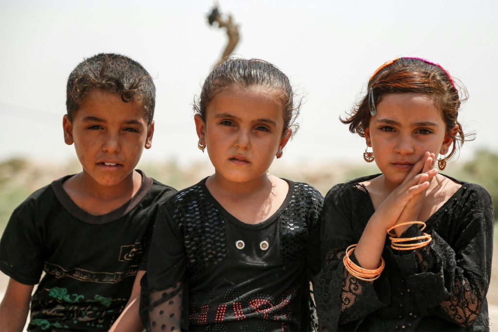 ثلاثة من أطفال العراقي ناجح فرحان السبعة في صورة ملتقطة في باحة منزلهم في قرية الزوية في جنوب العراق في التاسع من آب/أغسطس 2023 (ا ف ب)