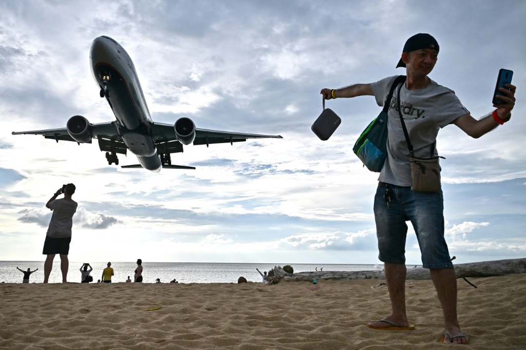 صورة ملتقطة في 18 تشرين الثاني/نوفمبر 2023 تظهر سائحا يلتقط صورة ذاتية على شاطئ ماي خاو فيما تستعد طائرة للهبوط في مطار بوكيت الدولي في جنوب تايلاند (أ ف ب)   