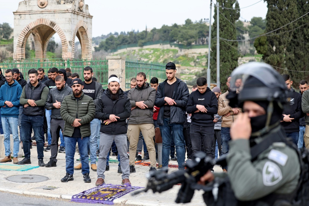 عنصر أمن إسرائيلي يقف بينما يؤدي مسلمون فلسطينيون صلا الجمعة في أحد شوارع القدس الشرقية في 23 شباط فبراير 2024 (ا ف ب)