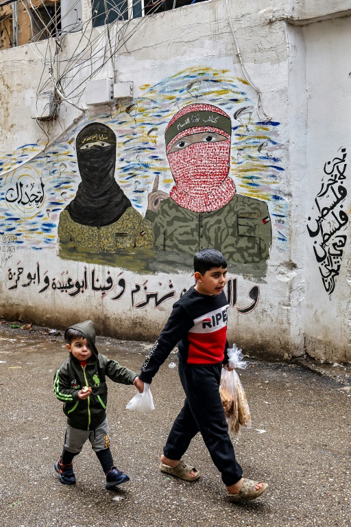 أطفال يسيرون أمام لوحة جدارية تصور مقاتلي كتائب القسام وكتائب القدس، الأجنحة المسلحة لحركتي حماس والجهاد الإسلامي الفلسطينيتين، مرسومة على جدار في مخيم للاجئين الفلسطينيين في الضاحية الجنوبية لبيروت (ا ف ب)