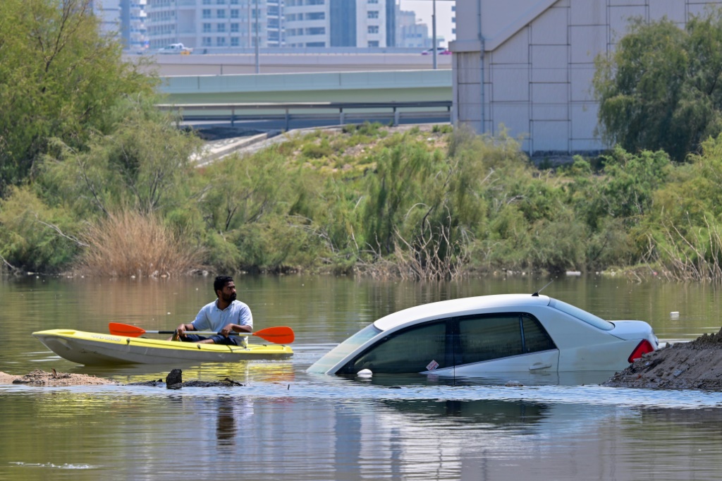 رجل يقود زورقه أمام سيارة تقطعت بها السبل في شارع غمرته المياه في دبي (ا ف ب)