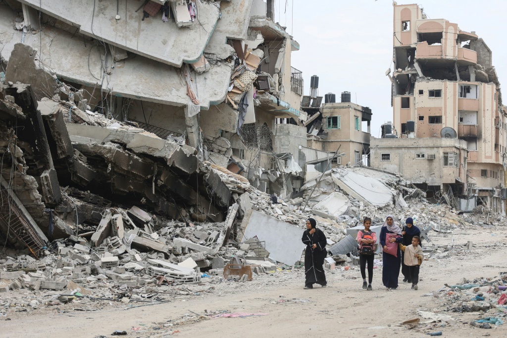 نساء وأطفال فلسطينيون يسيرون بجوار أنقاض المباني التي دمرها القصف الإسرائيلي في مدينة غزة في 8 نيسان أبريل 2024، وسط الحرب المستمرة بين إسرائيل وحركة حماس (ا ف ب)