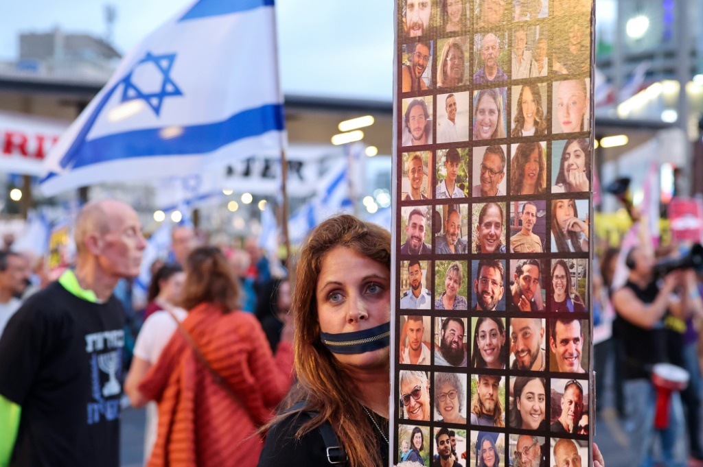 متظاهرة تحمل سحابًا على فمها تحمل صور الرهائن الإسرائيليين في مسيرة في تل أبيب تطالب الحكومة بإبرام اتفاق مع حماس لإطلاق سراحهم (أ ف ب)   