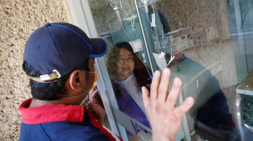 رجل يزور مصابة بـ«كورونا» من وراء زجاج عازل في مستشفى بمكسيكو سيتي أمس (رويترز)