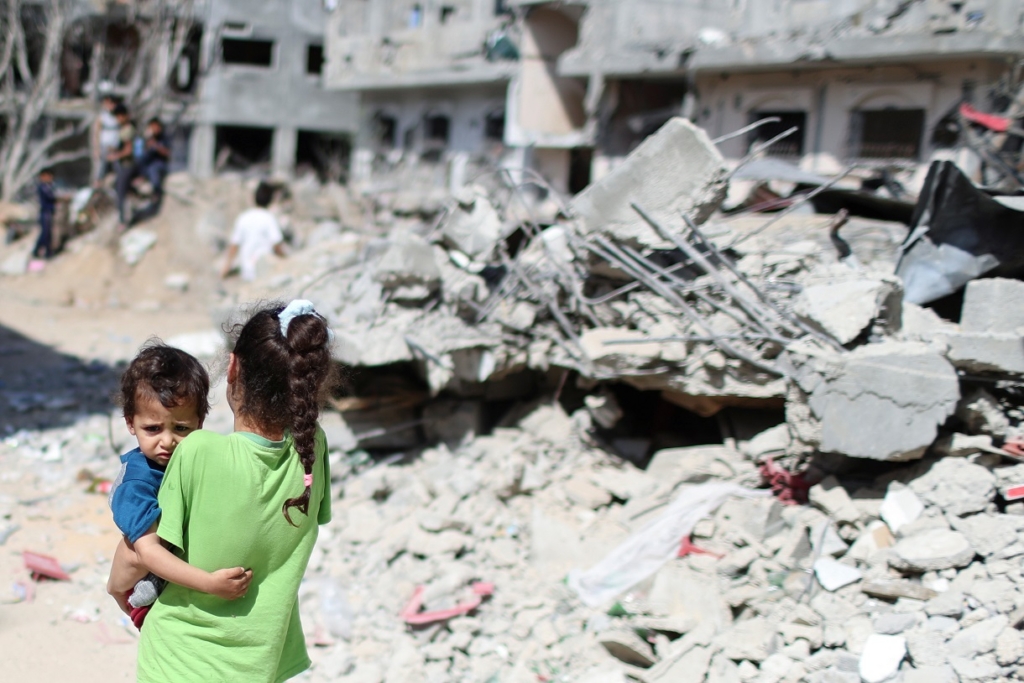 فتاة فلسطينية تحمل طفلاً أمام أنقاض منازلهم التي دمرتها الغارات الجوية الإسرائيلية على غزة