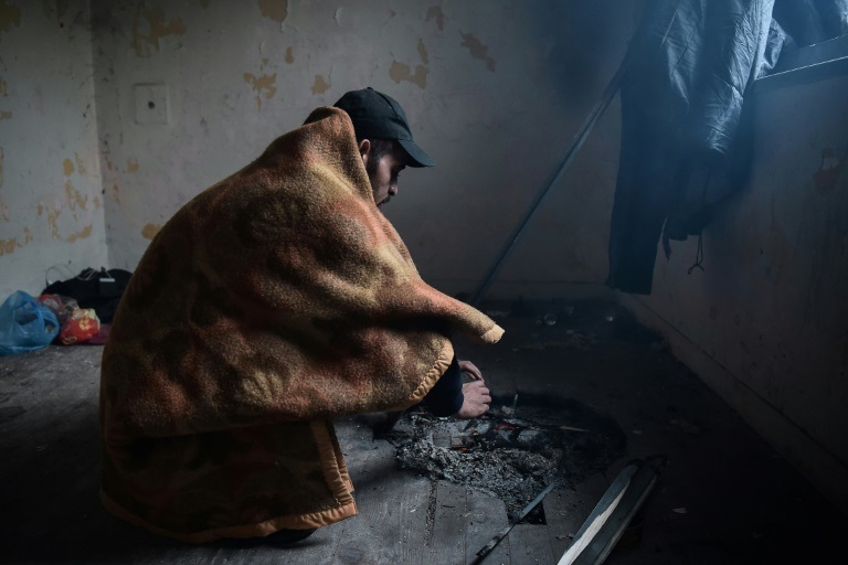 مهاجر يتدفّأ بغطاء قرب النار في منزل مهجور قرب الحدود بين اليونان ومقدونيا الشمالية في 18أكتوبر 2021(ا ف ب)