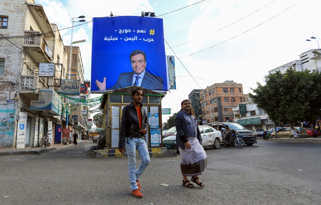 مارة يسيرون قرب صورة لوزير الإعلام اللبناني جورج قرداحي في صنعاء (أ ف ب)