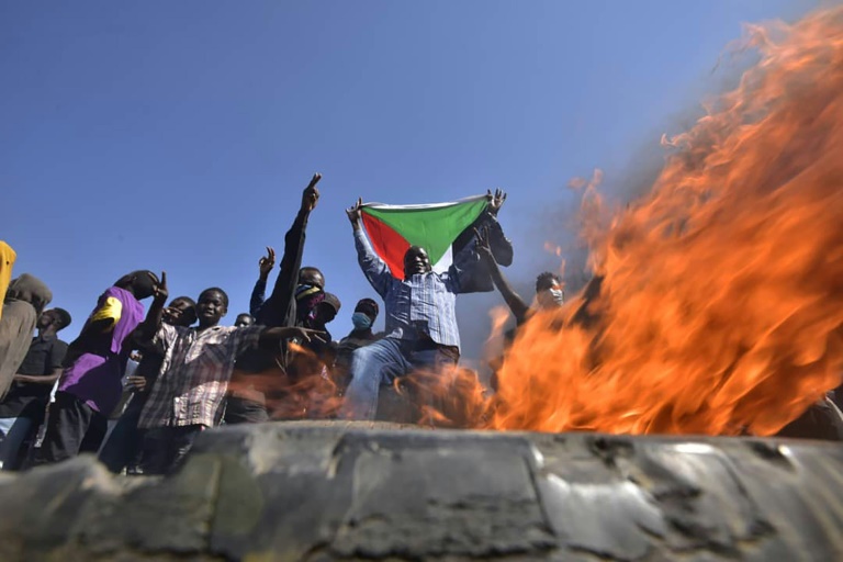 رحل يحمل علم السودان عند حاجز أُضرِمَت فيه النار بشرق الخرطوم في 13 تشرين الثاني/نوفمبر 2021 وسط احتجاجات ضد الانقلاب العسكري(ا ف ب)