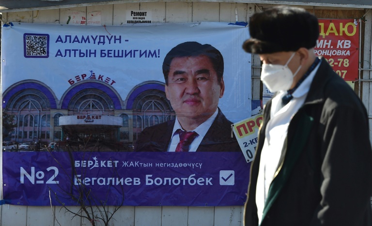 رجل واضعًا كمامة وماشيًا قرب لافتة عليها صورة مرشّح للانتخابات التشريعية في قرية تاش-دوبو البعيدة 25 كيلومترًا عن القرغيزستانية بشكيك في 24 تشرين الثاني/نوفمبر 2021(ا ف ب)