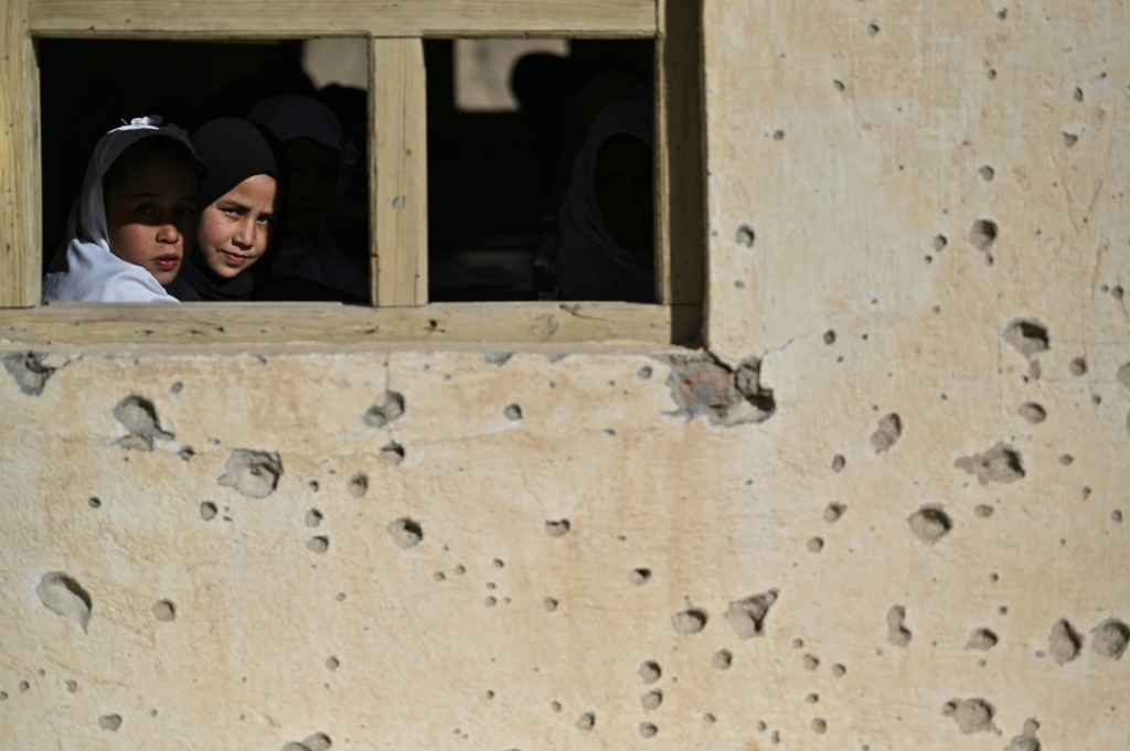 فتاتان خلف نافذة مدرستهما التي تحمل آثار رصاص في قرية آرزو بجنوب أفغانستان في 16 تشرين الثاني/نوفمبر 2021 (أ ف ب)