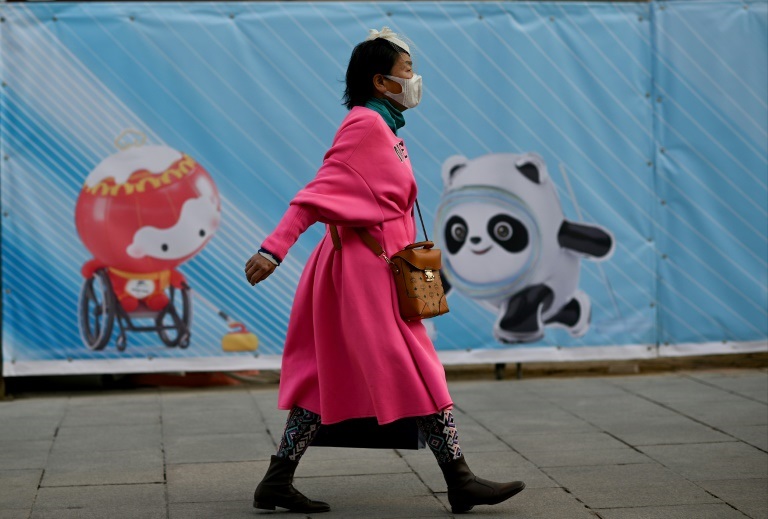  امرأة تمر أمام لافتة عليها تعويذات أولمبياد بكين، في بكين في 5 كانون الأول/ديسمبر 2021(ا ف ب)
