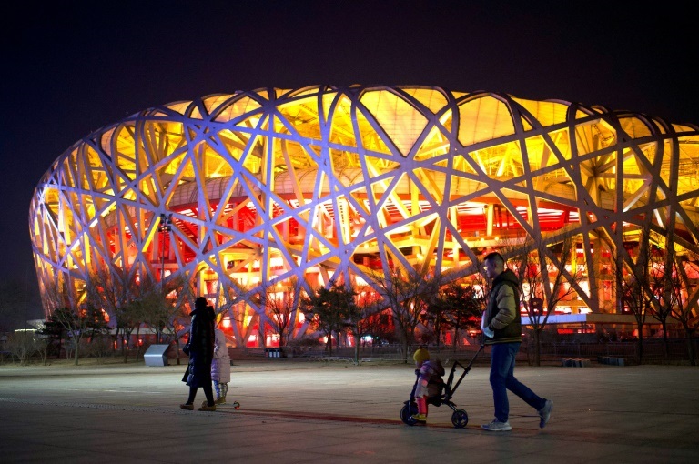صورة لأشخاص يمشون بجوار ملعب "عش الطائر" مكان حفل الافتتاح والختام في دورة الألعاب الأولمبية الشتوية 2022، في بكين في الرابع من شباط/فبراير 2021، قبل عام من افتتاحها( ا ف ب)