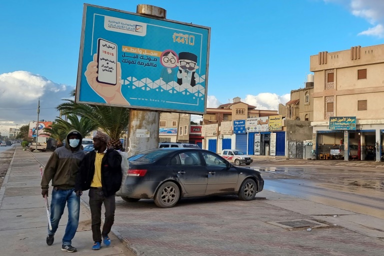 عمال بجوار لوحة انتخابية تدعو للمشاركة في الانتخابات في العاصمة الليبية طرابلس في 14 كانون الأول/ديسمبر 2021(ا ف ب)
