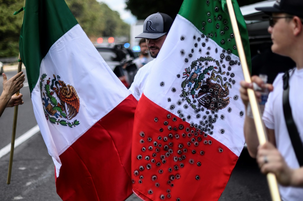 رجل يحمل علماَ مكسيكياَ فيه ثقوب ترمز إلى الرصاص خلال مسيرة من اجل السلام واحتجاجاً على موجة جرائم العنف (ا ف ب)