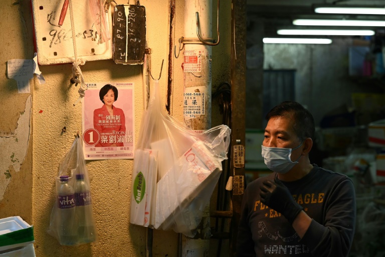 عامل يقف قرب ملصق إعلاني لحملة الانتخابات المحلية في هونغ كونغ في أحد أسواق المدينة في 8 كانون الأول/ديسمبر 2021(ا ف ب)