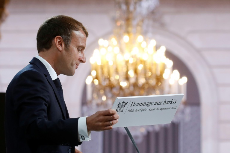 الرئيس الفرنسي إيمانويل ماكرون يحمل لوحا كتب عليه 