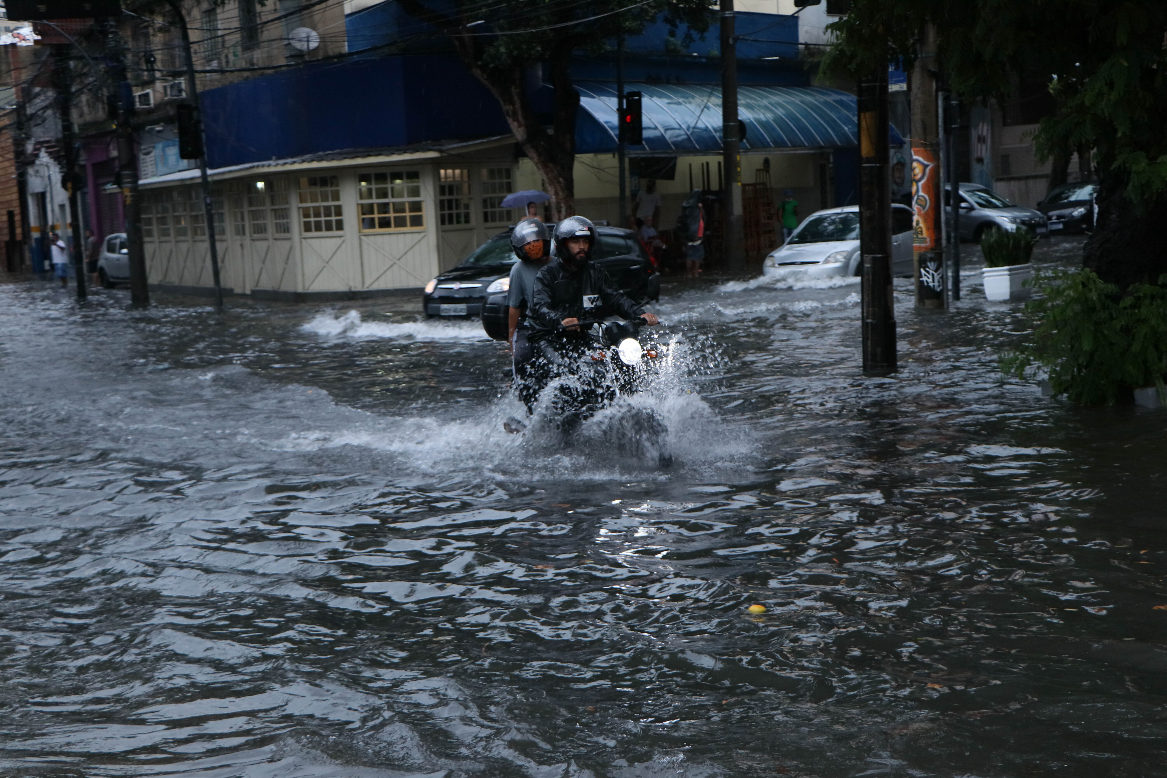  ريو دي جانيرو: رجلان يركبان دراجة نارية عبر شارع غمرته المياه في أعقاب الأمطار الغزيرة التي ضربت مدينة في ديسمبر 2021م ( د ب ا)