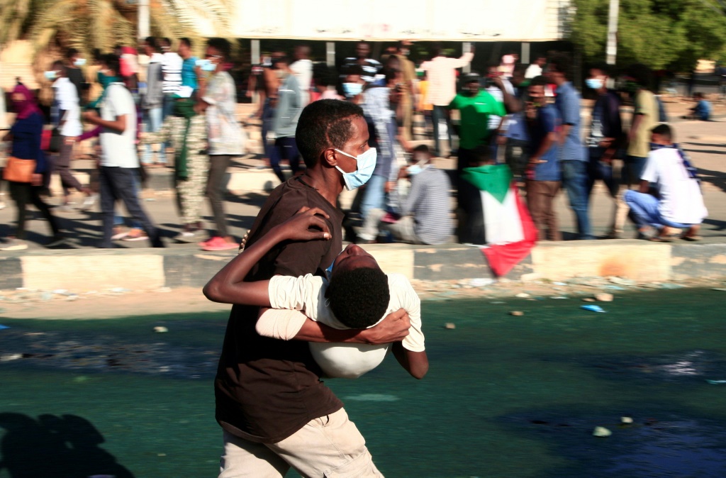 شاب سوداني يحمل متظاهرا مصابا وسط مواجهات مع قوات الامن في العاصمة الخرطوم في 25 كانون الأول/ديسمبر 2021 خلال احتجاجات مطالبة بعودة الحكم المدني (أ ف ب)   