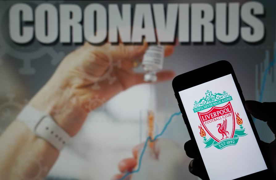 شعار نادي ليفربول لكرة القدم على هاتف محمول مع صورة توضيحية لفيروس كورونا على شاشة في الخلفية (د ب أ)