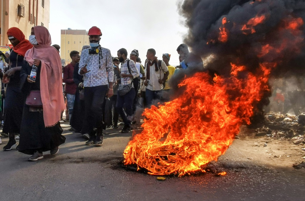    محتجون سودانيون يتظاهرون ويمرون بإطارات محترقة في الخرطوم في السادس من كانون الثاني/يناير 2022 (أ ف ب)