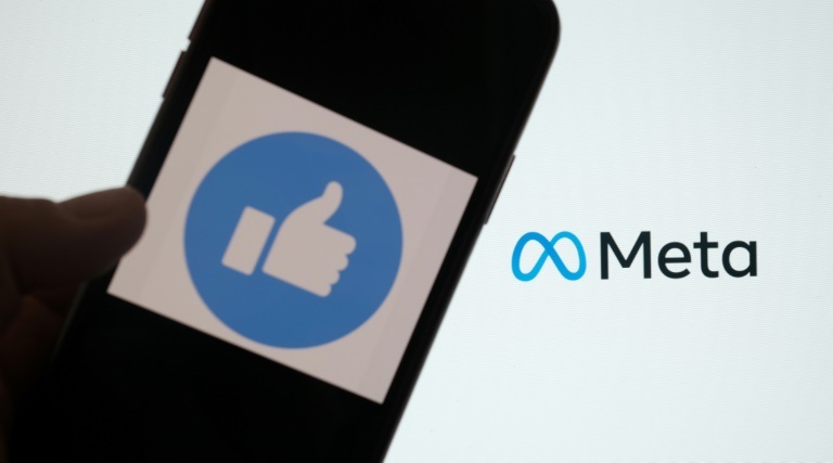شخص يستخدم فيسبوك على هاتف ذكي بينما يظهر شعار شركة "ميتا" على شاشة كمبيوتر أمامه، الصورة التُقطت في 28 تشرين الأول/أكتوبر 2021 (ا ف ب)