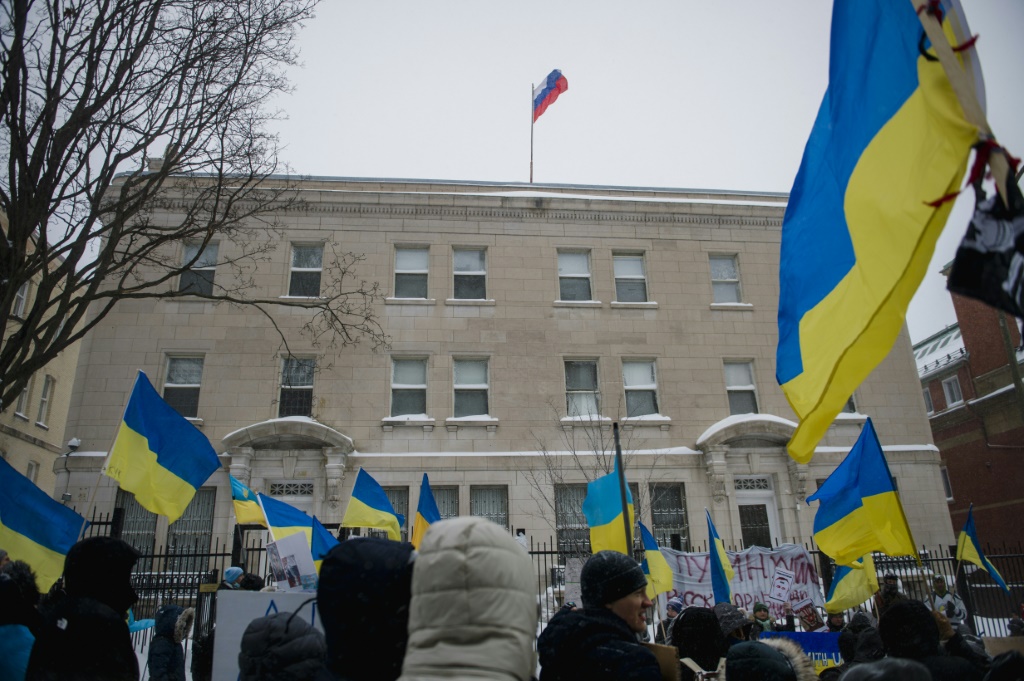 يظهر العلم الروسي فوق القنصلية الروسية في مونتريال بينما يلوح المتظاهرون بالأعلام الأوكرانية (أ ف ب)