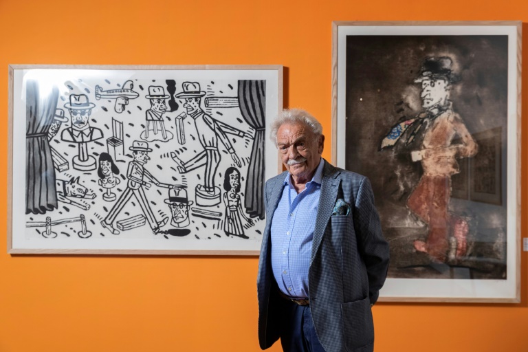 الرسام والنحات الأرجنتيني انطونيو سيغي أمام انثتين من لوحاته خلال معرض لأعماله في المكتبة الفرنسية في باريس في 5 حزيران/يونيو 2019 (اف ب)