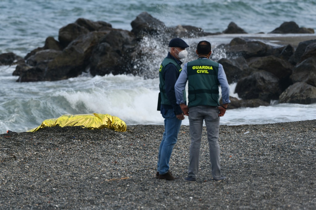 عنصران من شرطة الحماية المدنية الإسبانية يقفان على مقربة من جثة مغطاة، على شاطئ في سبتة في 21 أيار/مايو 2021 (أ ف ب)