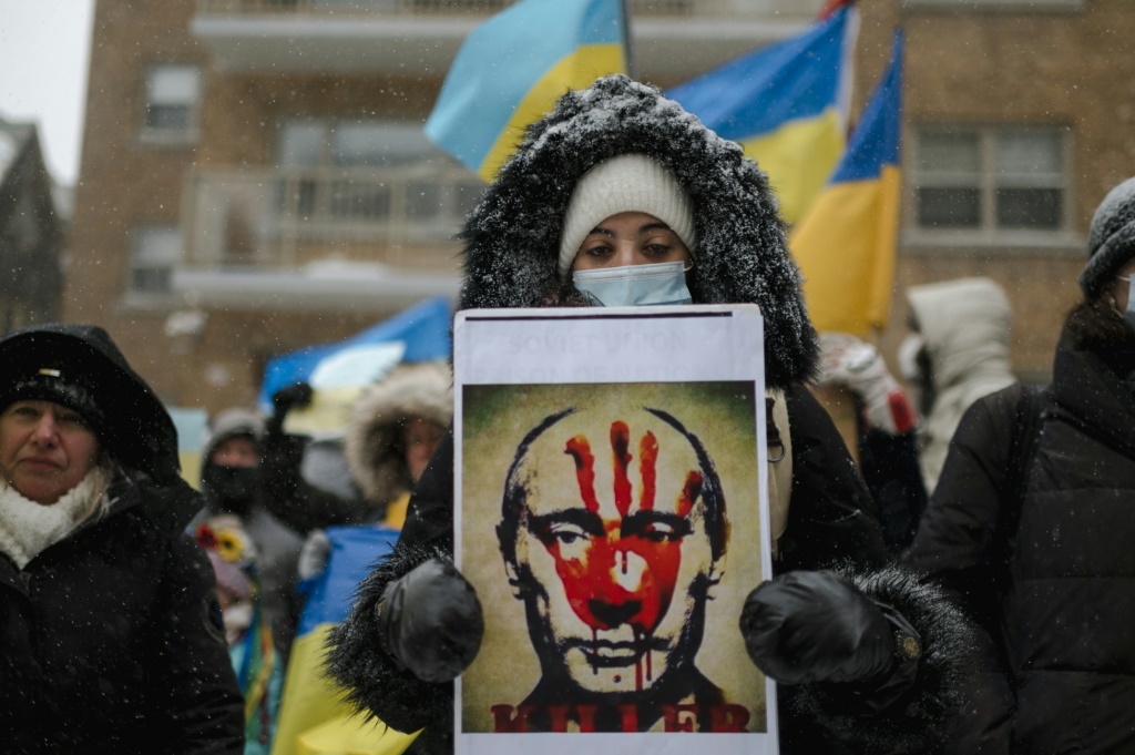امرأة تحمل صورة الرئيس الروسي فلاديمير بوتين ويدها ملطخة بالدماء بينما أعضاء الجالية الأوكرانية في كندا وأنصار يحتجون خارج القنصلية الروسية في مونتريال (أ ف ب)