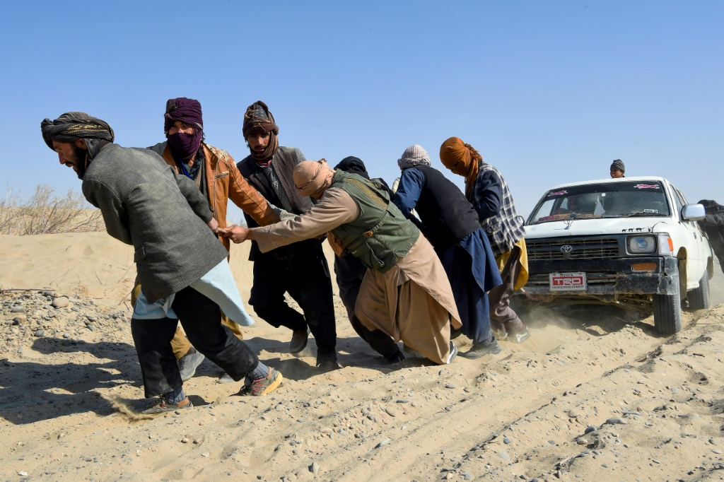 في الصورة الملتقطة في 17 شباط/فبراير 2022 يجر مهاجرون أفغان شاحنة صغيرة عالقة في طريق صحراوي عند الحدود الأفغانية الإيرانية في نمروز (أ ف ب)