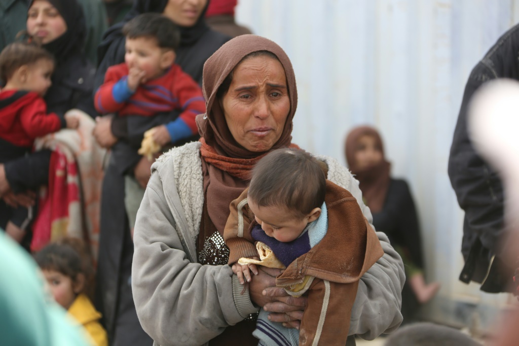 سيدة سورية تحمل طفلًا عبر ممر يسيطر عليه النظام عام 2018 (أ ف ب)