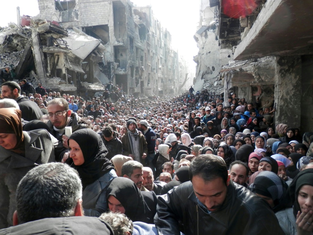 سكان ينتظرون الطعام في نقطة توزيع تابعة للأمم المتحدة في مخيم اليرموك للاجئين جنوب دمشق عام 2014 (ا ف ب)