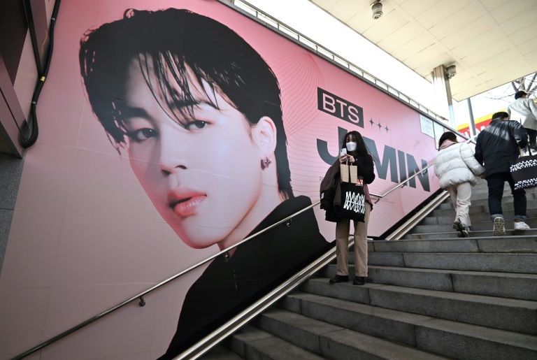 امرأة تلتقط صوراً أمام ملصق يحمل صورة أحد أعضاء فرقة "بي تي إس" في محطة مترو أنفاق بالقرب من ملعب سيول الأولمبي في 10 آذار/مارس 2022 قبل الحفلة الموسيقية للفرقة (ا ف ب)