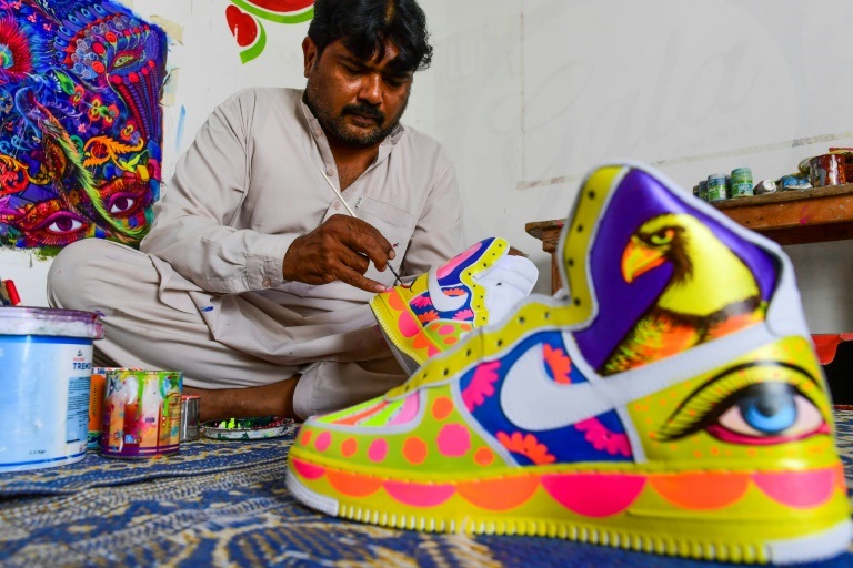 الفنان الباكستاني حيدر علي يلوّن زوجي أحذية رياضية ليحولهما قطعة فنية في الاستوديو الخاص به في كراتشي في 28 شباط/فبراير 2022 (ا ف ب)