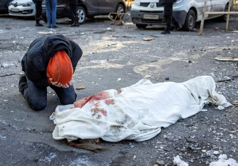 شخص يبكي إلى جانب جثة ملفوفة بقماش أبيض قرب مبنى سكني أُصيب بشظايا صاروخ في كييف في 17 آذار/مارس 2022 (ا ف ب)