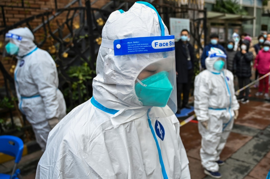 عمال يرتدون بزات واقية فيما الناس ينتظرون للخضوع لفحص تشخيص الإصابة بكوفيد-19 في مجمع سكني في شانغهاي في 18 آذار/مارس 2022(ا ف ب)