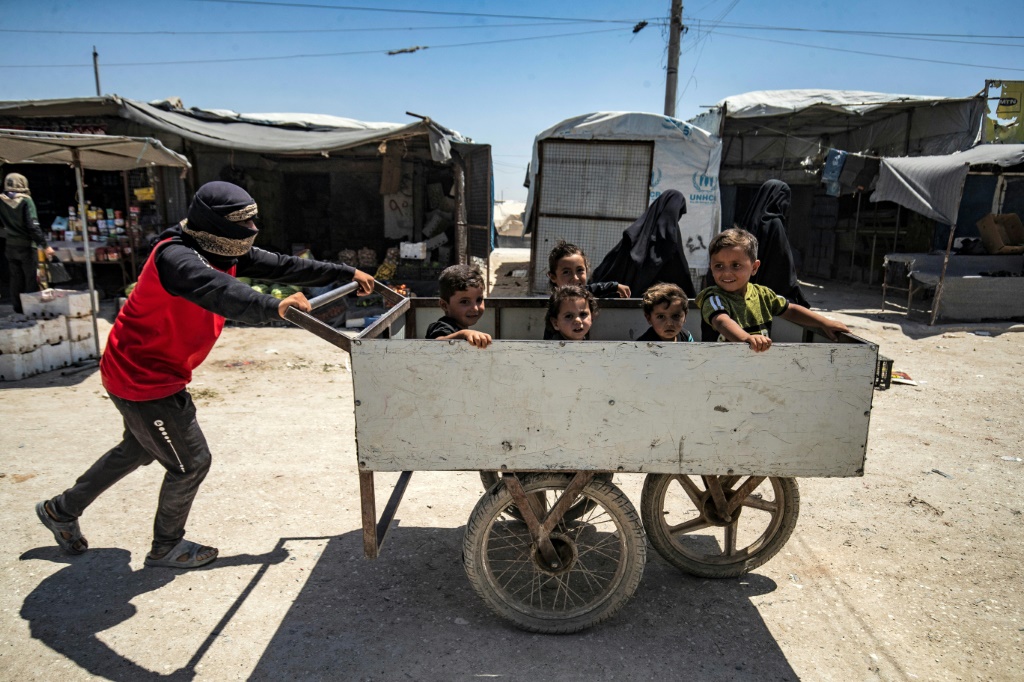رجل يدفع عربة يجلس داخلها أطفال في مخيم الهول في شمال شرق سوريا في 23 حزيران/يونيو 2021(ا ف ب)