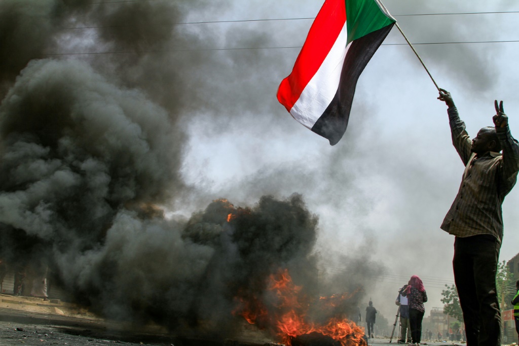 متظاهر يرفع العلم السوداني قرب اطارات تحترق في العاصمة الخرطوم(ا ف ب)