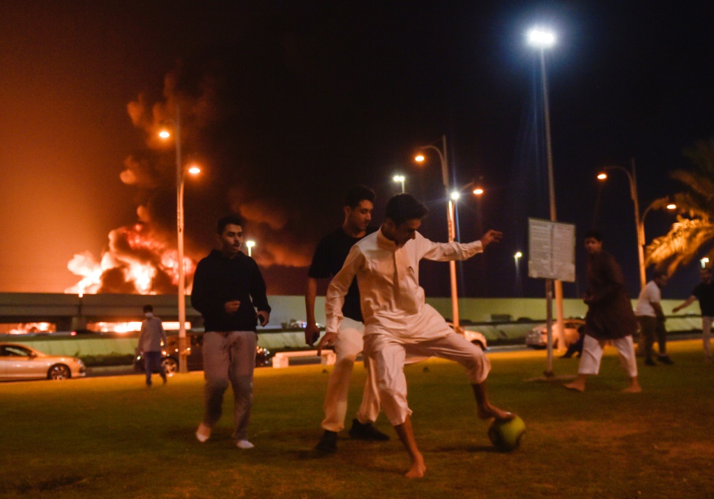 شباب يلعبون كرة القدم في مدينة جدة السعودية الساحلية على البحر الأحمر فيما يتصاعد الدخّان وألسنة اللهب من منشأة تابعة لشركة أرامكو النفطية خلفهم في 25 آذار/مارس 2022(ا ف ب)