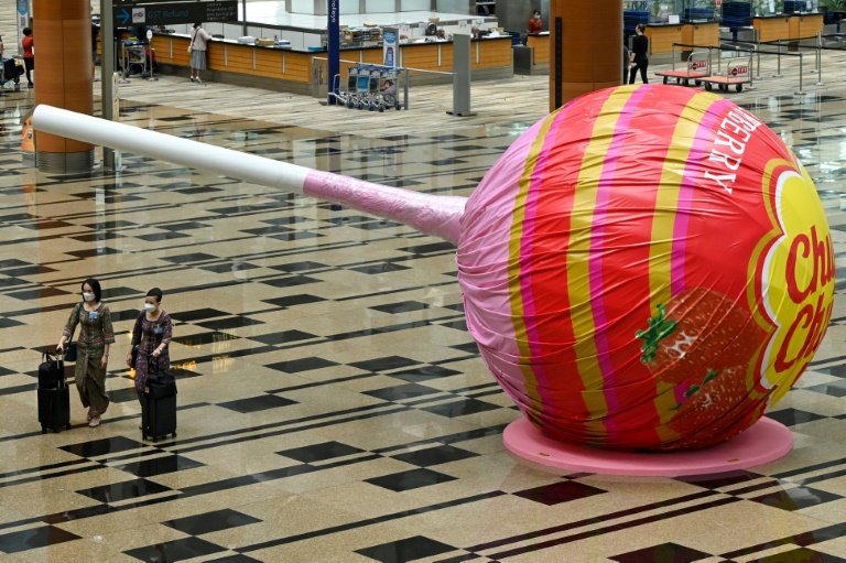   مضيفات طيران يمشين أمام مصاصة عملاقة في مطار شانغي في سنغافورة ( أ ف ب)