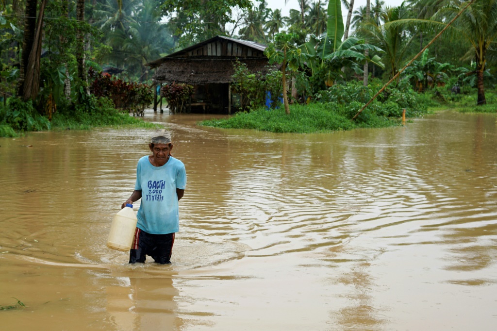  رجل يمشي على طريق غمرته المياه قرب منزله في بلدة أبويوغ في منطقة ليتي في جنوب الفيليبين في 11 نيسان/أبريل 2022 (ا ف ب)