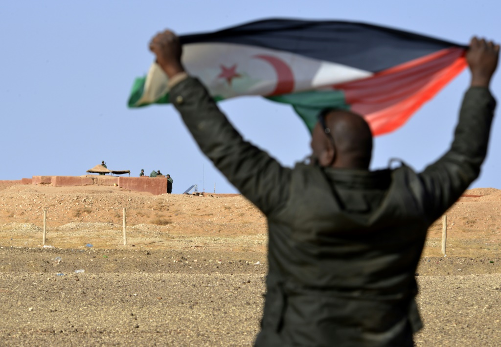 رجل صحراوي يرفع علم بوليساريو في منطقة المحبس امام جنود مغاربة يراقبون الجدار الفاصل بين الصحراء الغربية والمغرب في 03 شباط/فبراير 2017(ا ف ب)