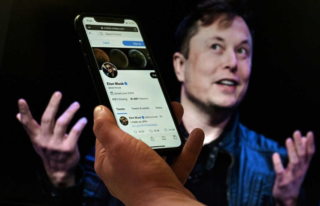 هاتف محمول يظهر على شاشته حساب إيلون ماسك عبر تويتر فيما تظهر في الخلفية صورة للملياردير في واشنطن في 14نيسان/أبريل 2022.(ا ف ب)