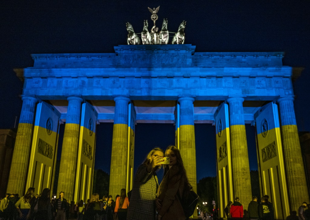 امرأتان تلتقطان صورًا شخصية أمام بوابة براندنبورغ التاريخية المضاءة بألوان العلم الأوكراني في برلين في 9 أيار/مايو 2022 (أ ف ب)