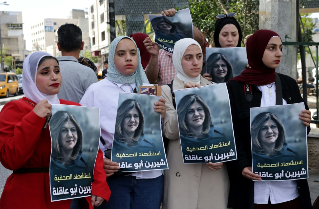فلسطينيون يحملون ملصقات تصور صحفية الجزيرة المخضرمة شيرين أبو عقله ، في مدينة الخليل بالضفة الغربية (أ ف ب)