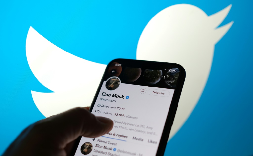 حساب إيلون ماسك في تويتر يظهر على شاشة أحد الهواتف على خلفية تبيّن رمز تويتر، الصورة التُقطت في لوس أنجليس في 13 أيار/مايو 2022 (ا ف ب)