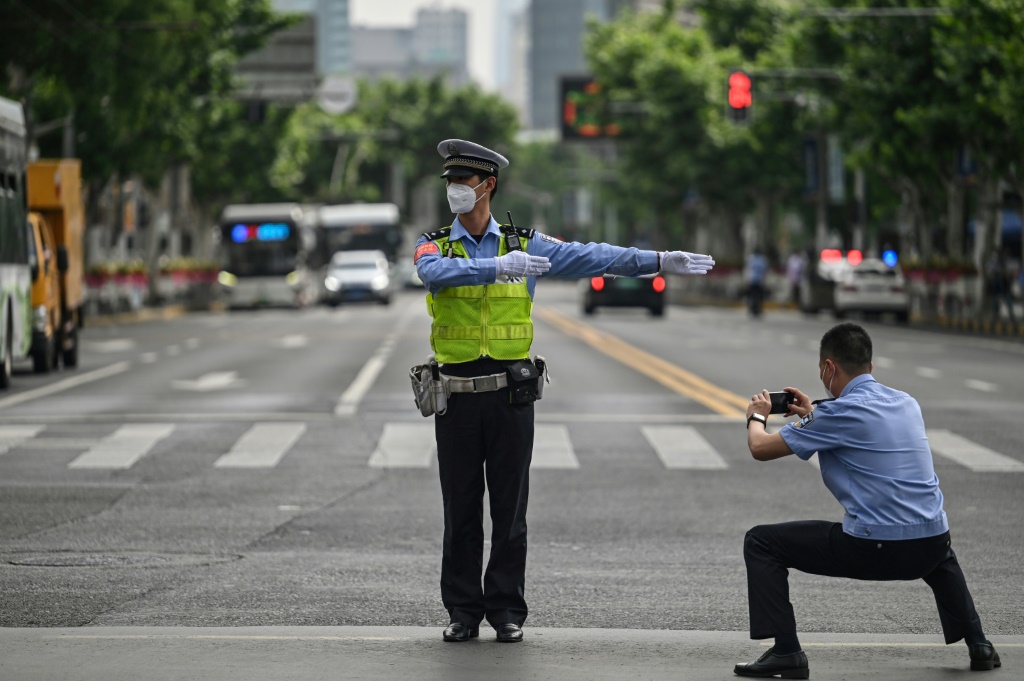 شرطي يلتقط صوراً لشرطي آخر ينظم السير في مدينة شنغهاي بعد انتهاء فترة حجر صحي دامت شهرين في 1 حزيران/يونيو 2022(ا ف ب)