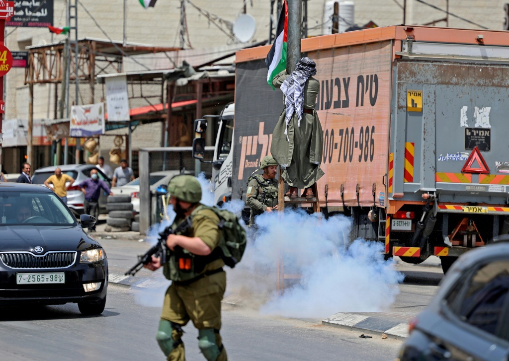    فلسطيني يحيط به جنود إسرائيليون يعلّق علا إسرائيليا في حوارة في الضفة الغربية المحتلة في 29 أيار/مايو 2022 (أ ف ب)