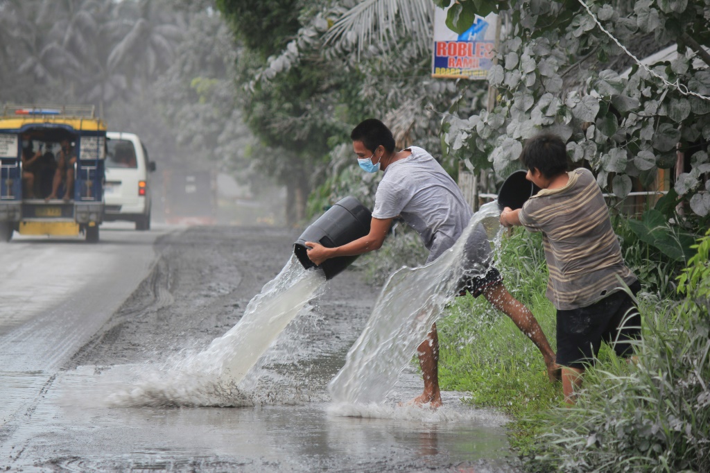 يعملان على تنظيف الرماد من أمام منزلهما في منطقة سورسوغون في الفيليبين بعد ثوران بركان بولوسان في 5 حزيران/يونيو 2022 (ا ف ب)